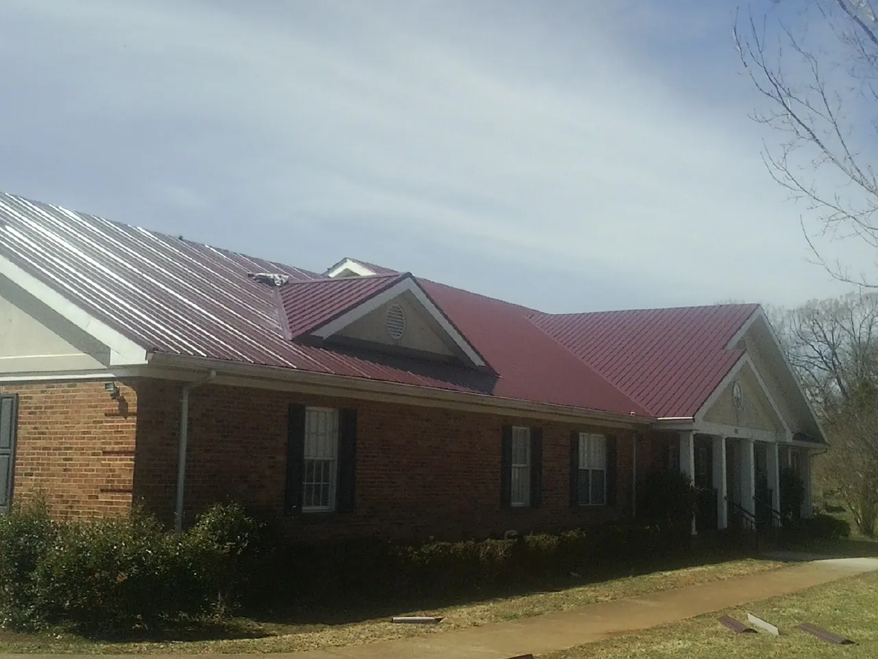Red metal roof with gabled entries on a long brick building, from a Hail Damage Roof Repair job in Hanahan
