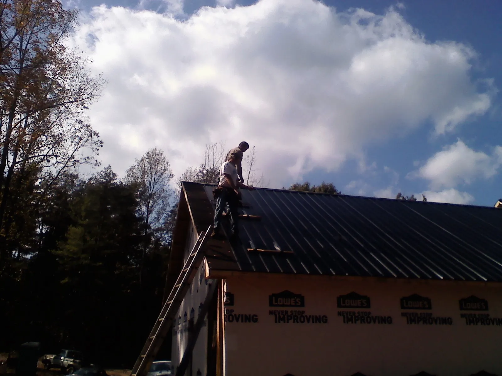 Roofer fastening dark metal panels high against a cloudy sky, from a Roof Inspection job in Hanahan
