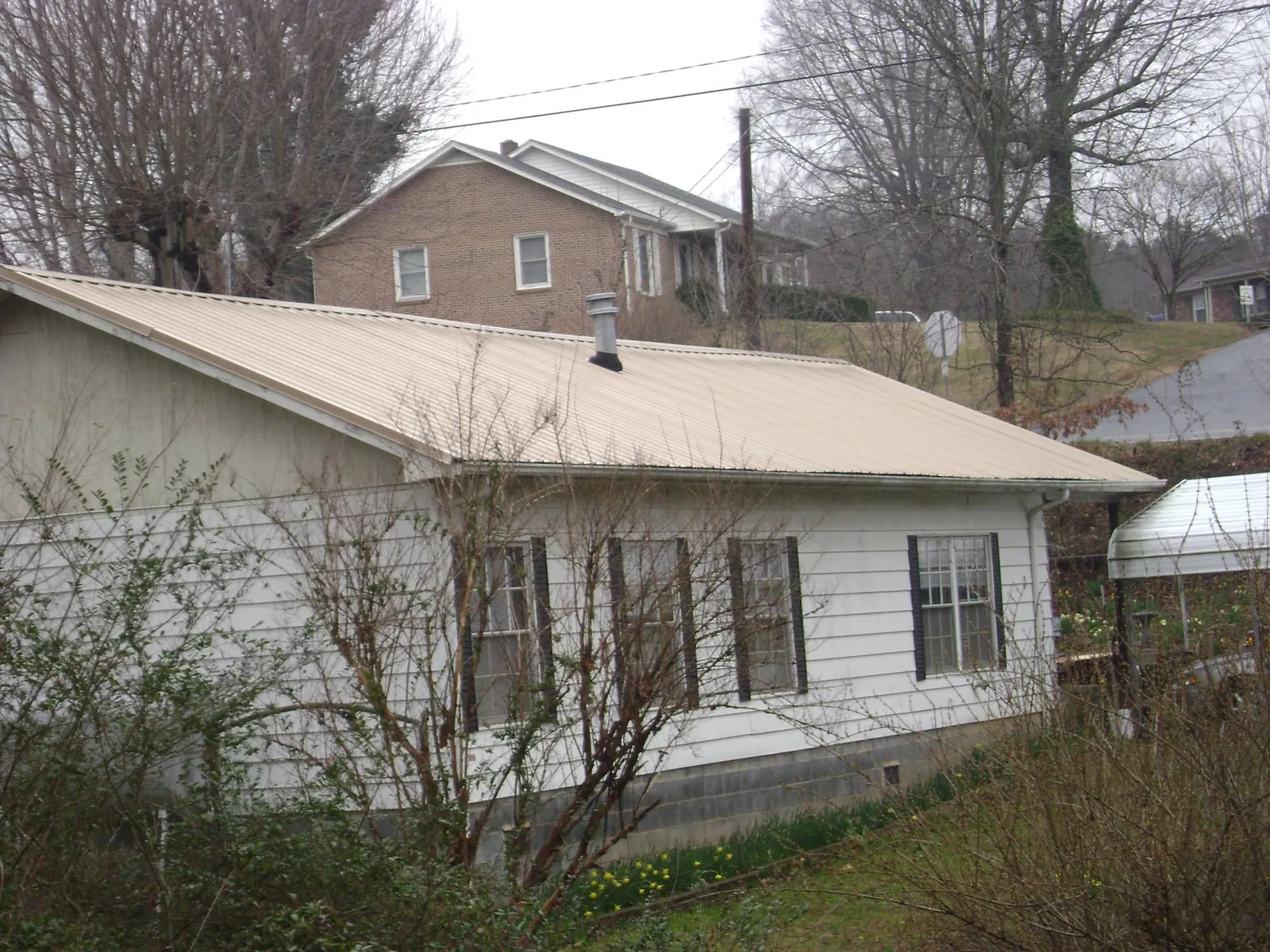 Tan metal roof on a white sided house set into a hillside — Commercial Roofing by Roofing Brothers in Hanahan